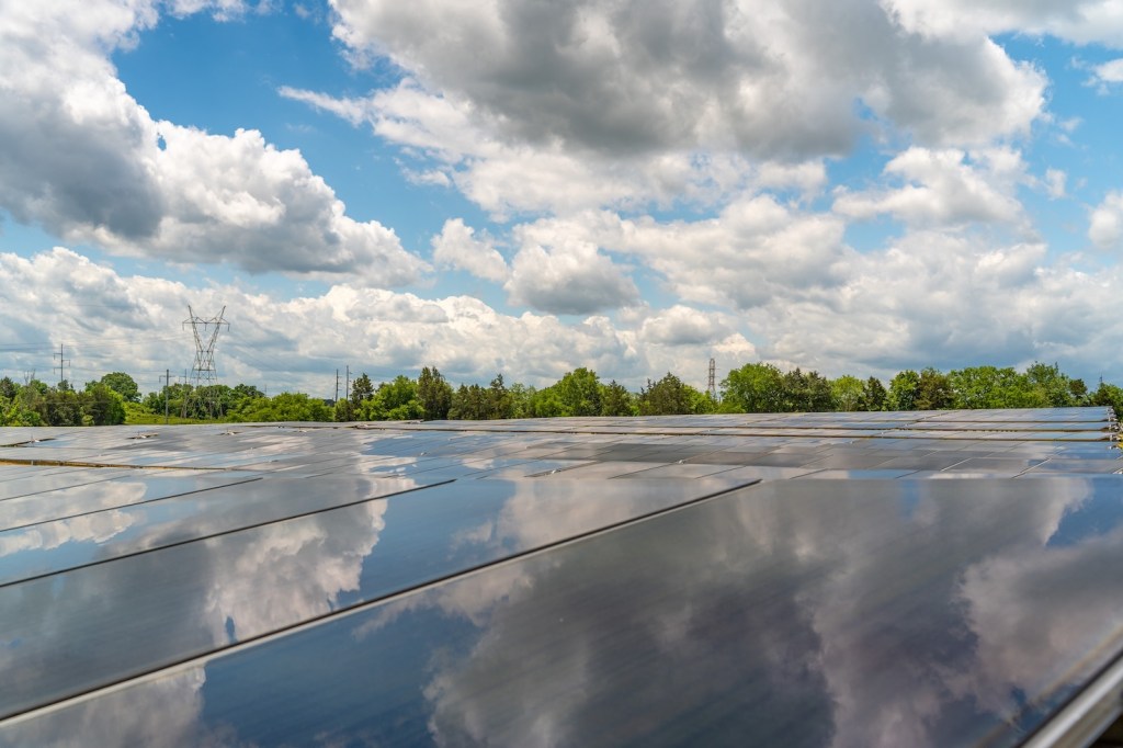 Solar panels under a blue sky with clouds.